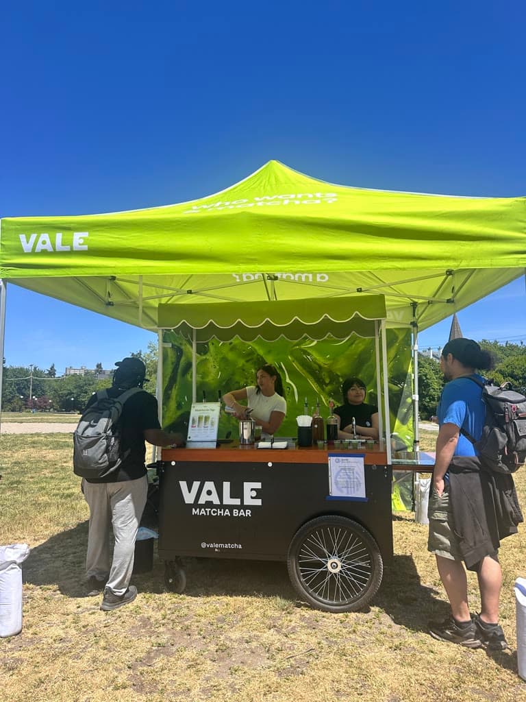 Vale Matcha Bar cart under a lime canopy at Cal Anderson Park in Capitol Hill, Seattle, with baristas pouring matcha and customers at the counter