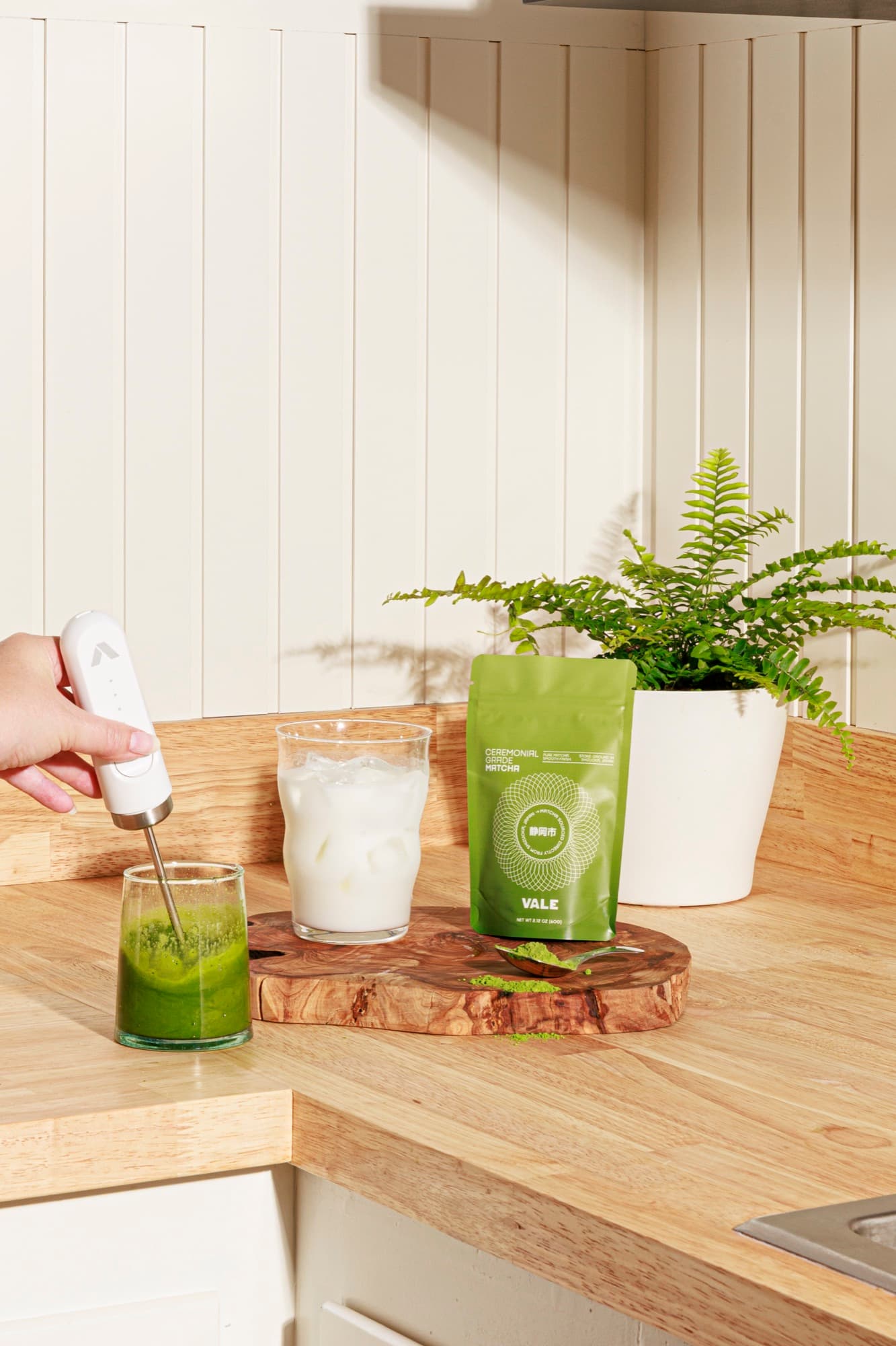 Hand frothing ceremonial matcha with a milk frother on a wooden cutting board