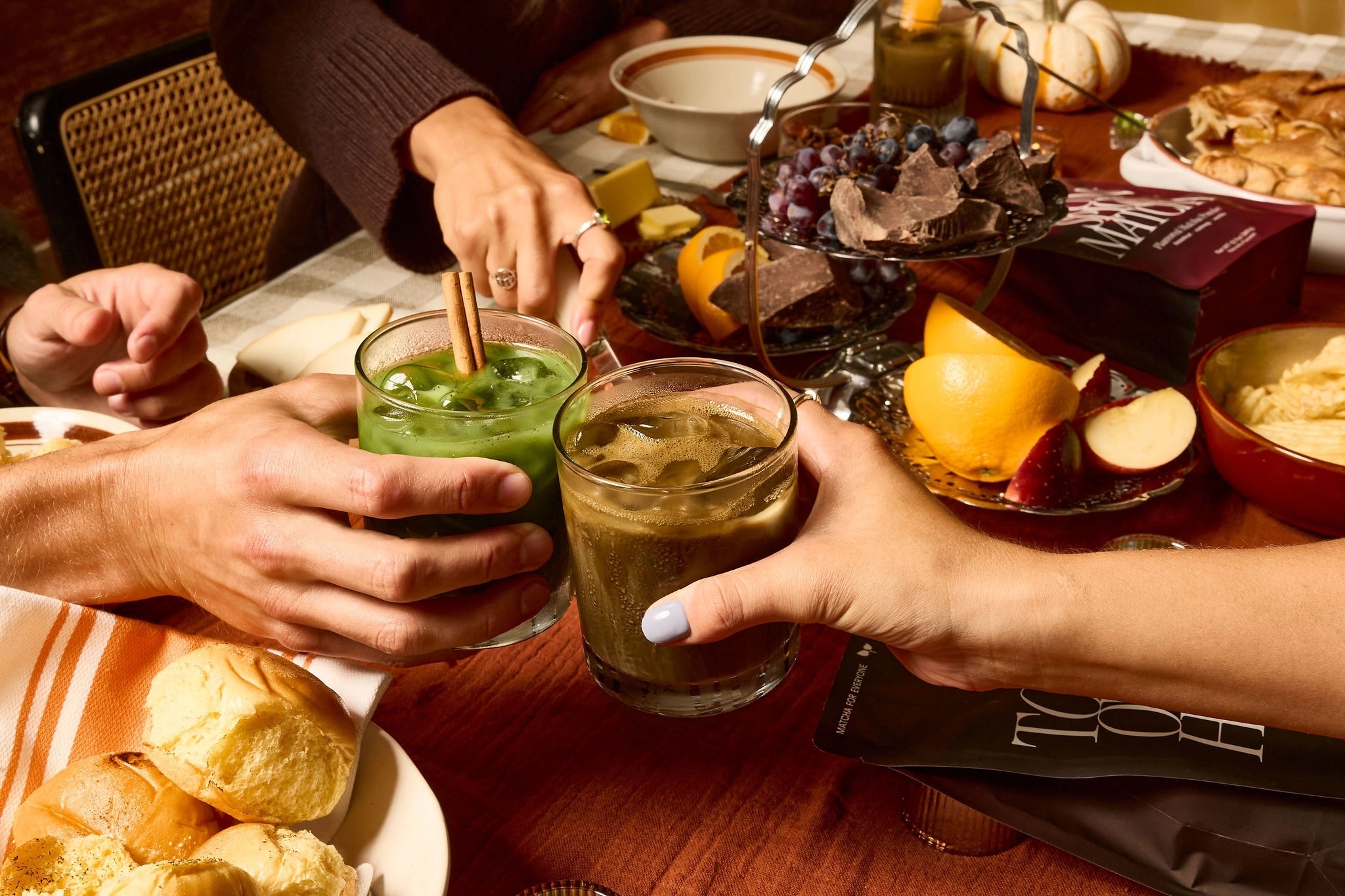 Friends toasting with iced Autumn Spice Matcha and Toasted Orange Hōjicha over a fall table