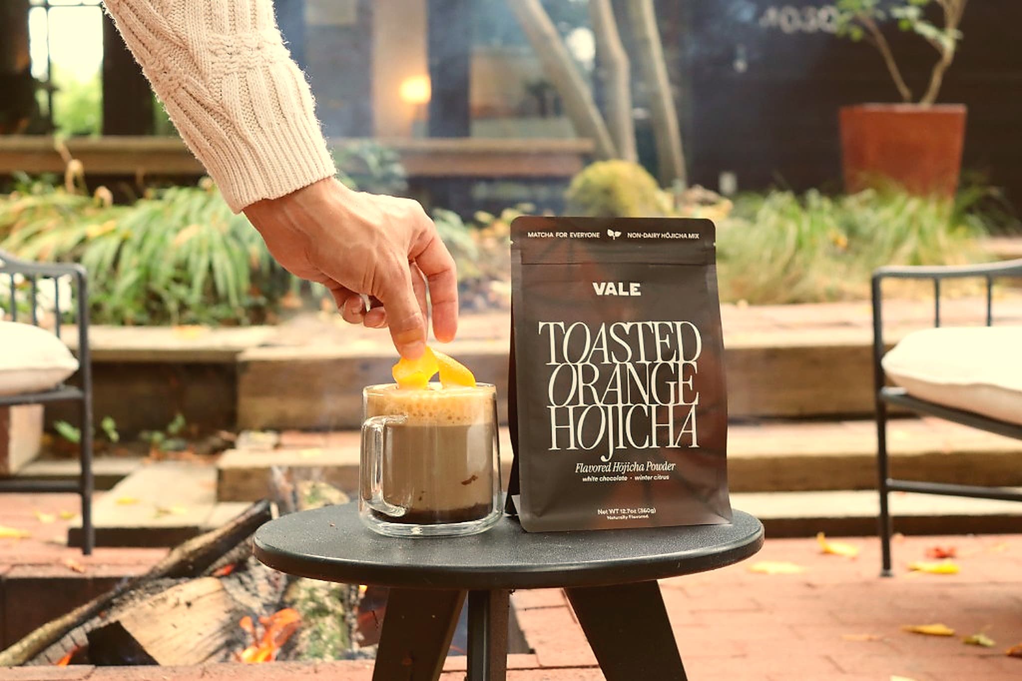 Hot hojicha latte with an orange twist beside a fire pit
