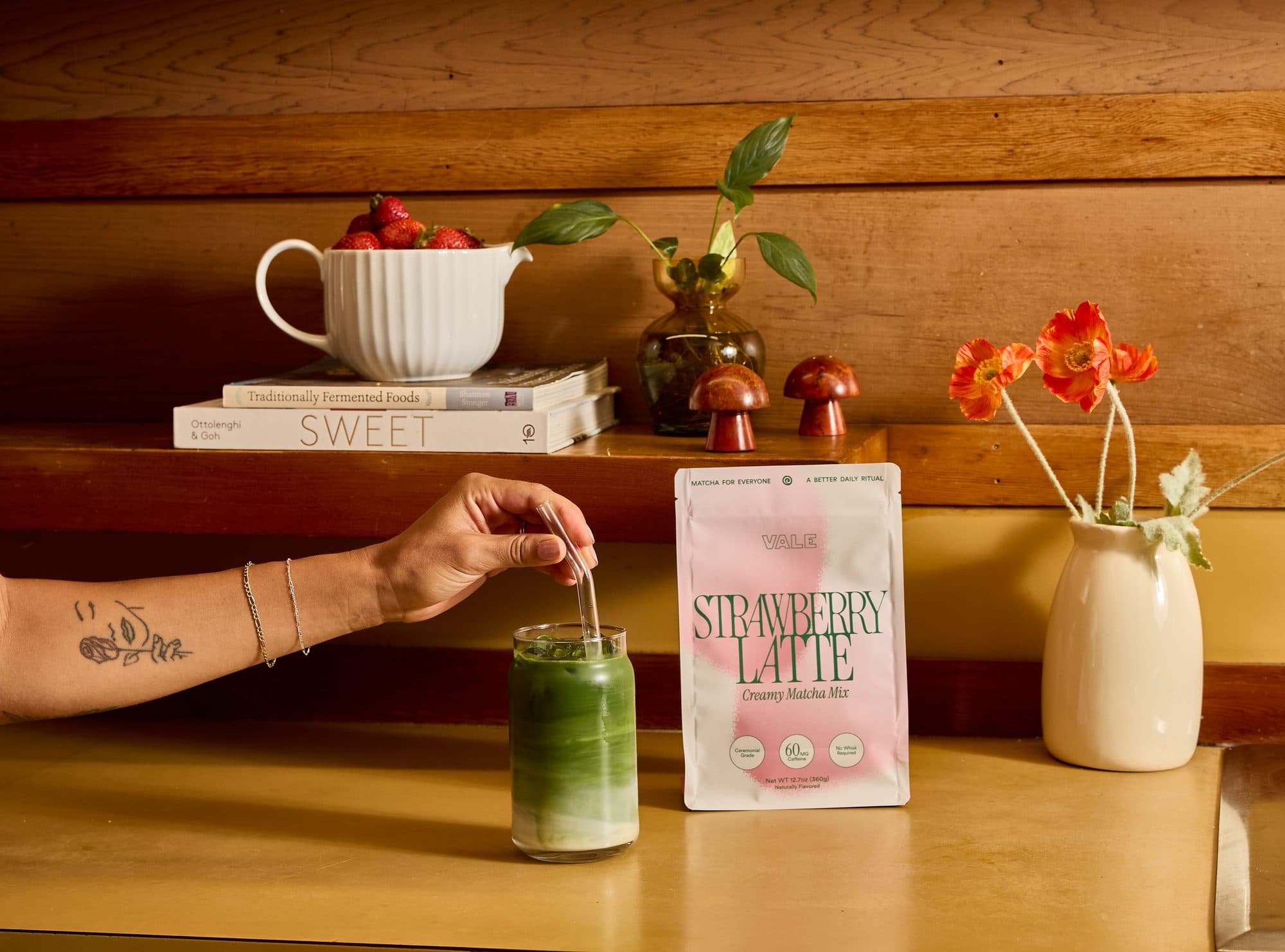 Stirring an iced latte beside Strawberry Matcha and fresh strawberries